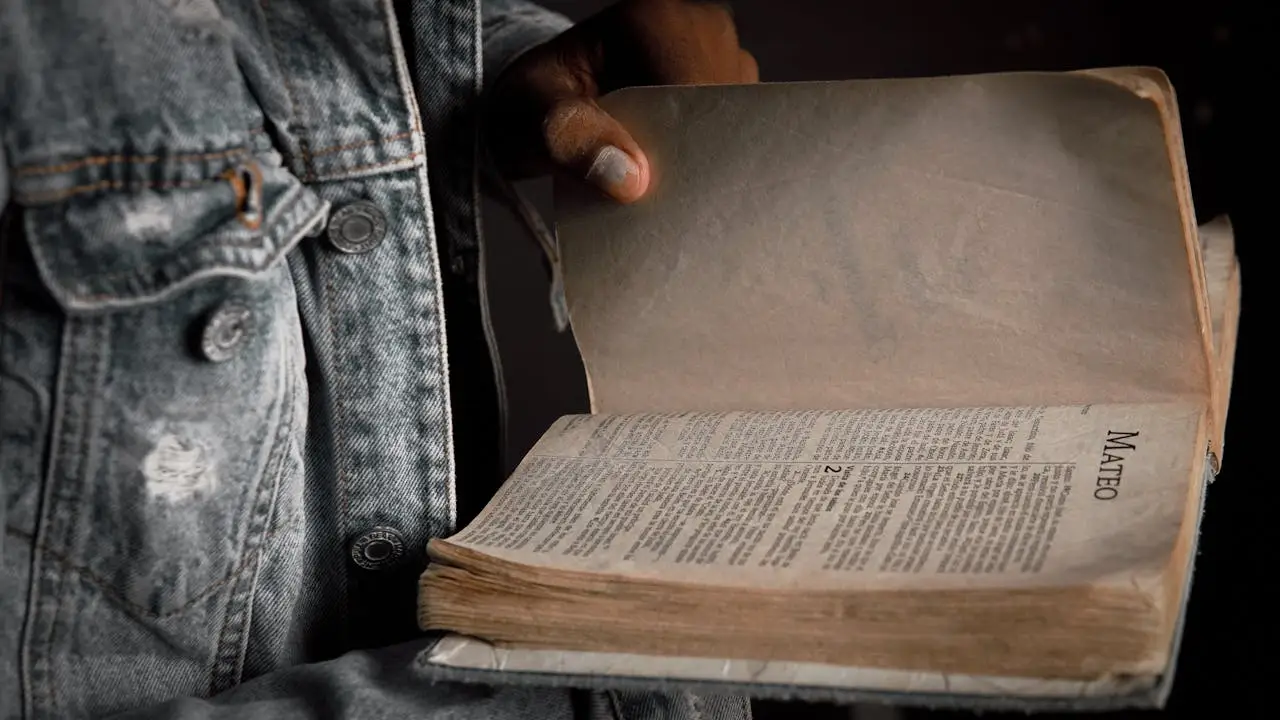 A person in a denim jacket holding an open Bible to the book of Matthew.