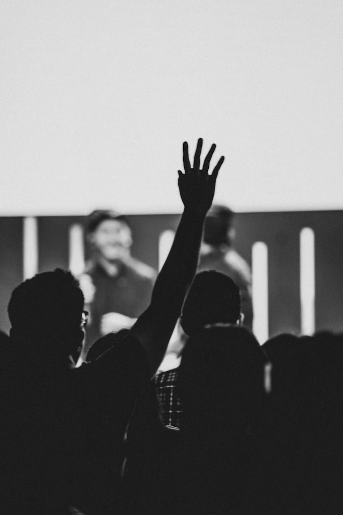 Black and white image of a person raising their hand during an indoor worship or community event.